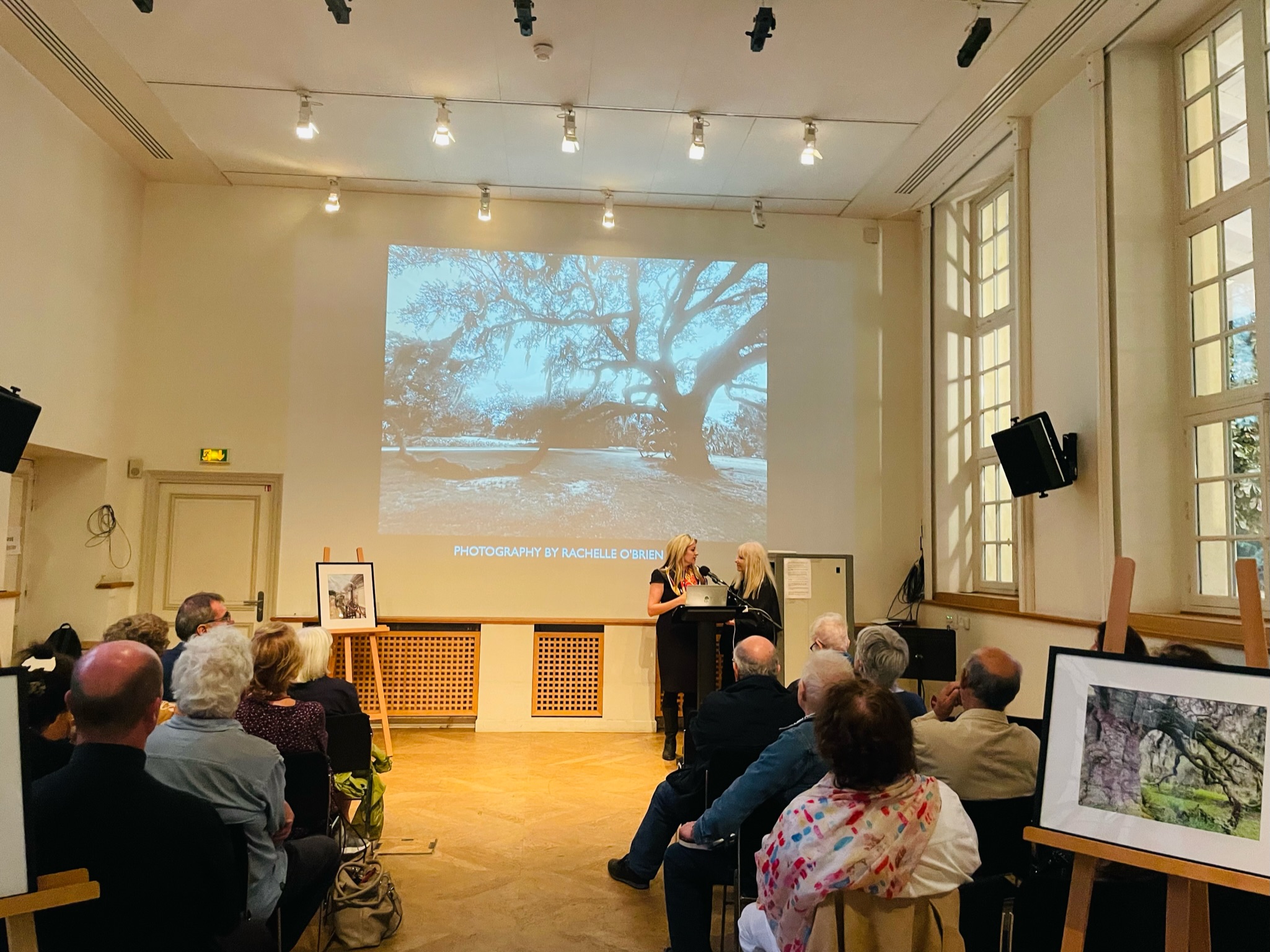 Rosary and Rory speaking to an audience in front of a projection of a large tree