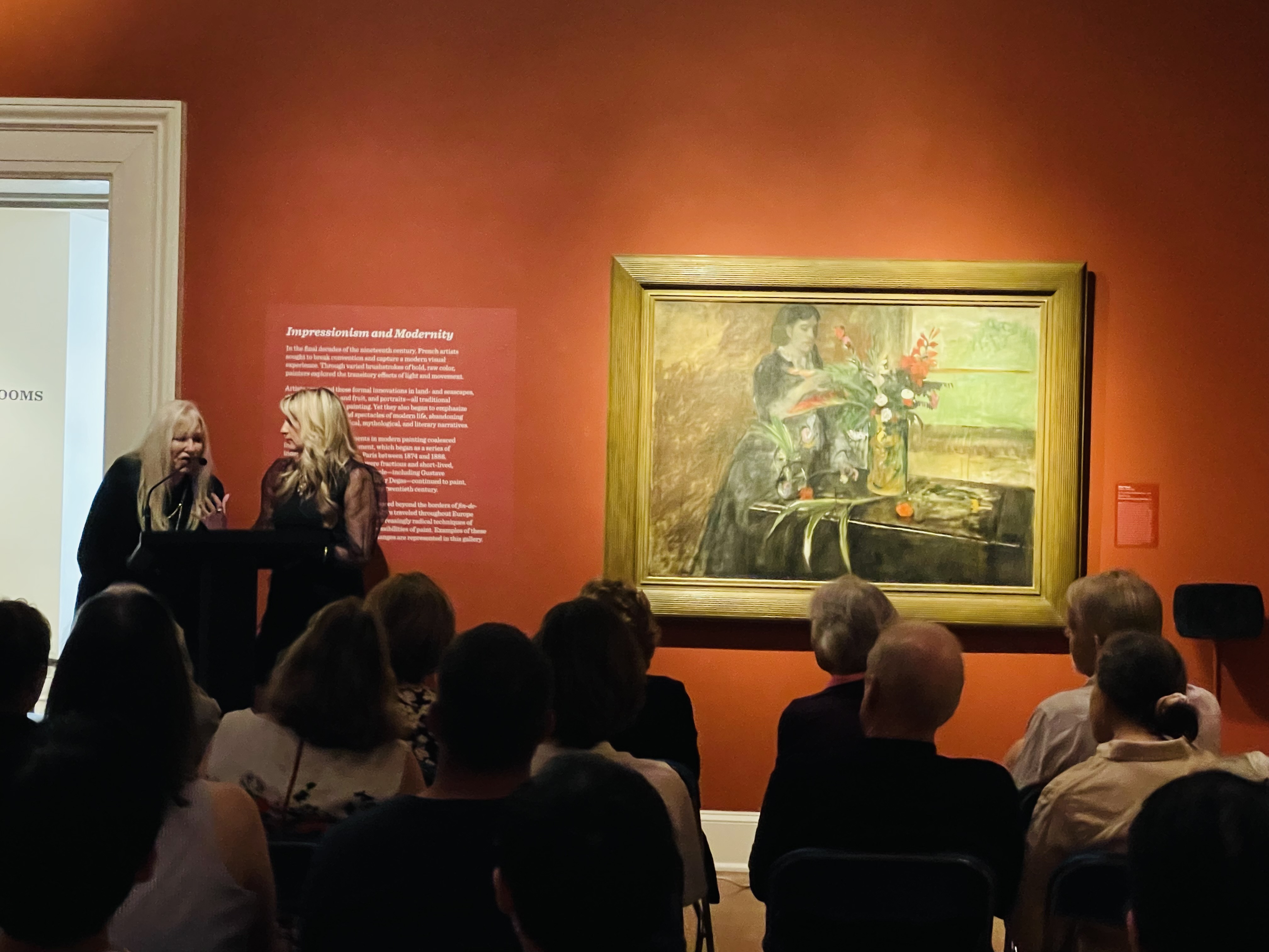 Rosary and Rory speaking to an audience in front of a large painting